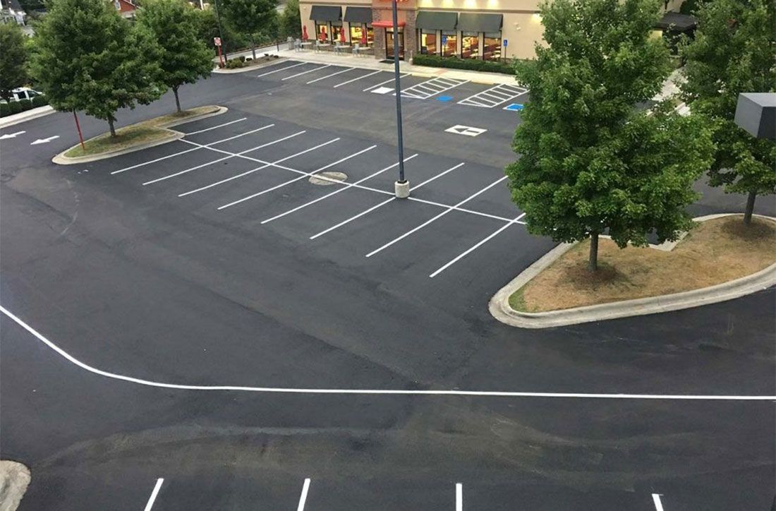 Empty asphalt parking lot with white lines and a few trees near a building.