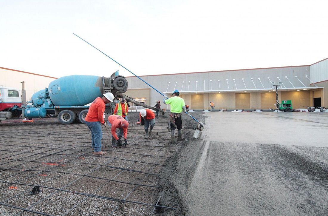 Construction workers pouring concrete from a truck onto a prepared surface, near a building.