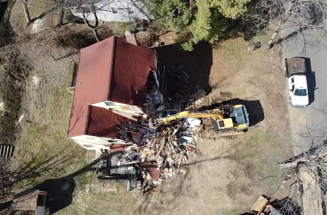 Aerial view of a house being demolished by an excavator.